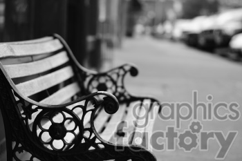 A black and white image depicting a wooden and wrought-iron bench, with intricate floral designs, on a blurred city sidewalk.