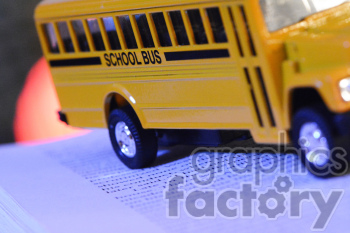 Clipart image of a miniature yellow school bus placed on an open book, highlighting themes of education and transportation.