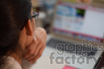 An individual wearing glasses is viewed from behind while they look at a laptop screen showing a blurred webpage.