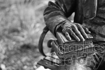 A close-up image of a bronze statue showing a hand resting on a stack of books. The artistic details of the sculpture are highlighted in black and white tones.