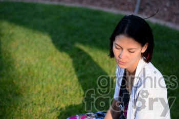 Image of a woman sitting on green grass, looking down with a contemplative expression.