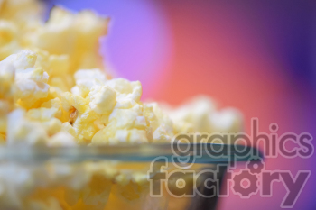 Close-up view of buttered popcorn in a glass bowl with a colorful blurred background.