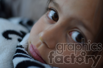 Close-up image of a child's face with brown eyes, lying down with a white and black patterned blanket.