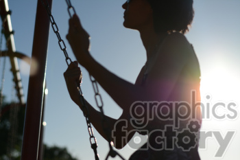 Silhouette of a person holding onto playground swing chains with the sun in the background.
