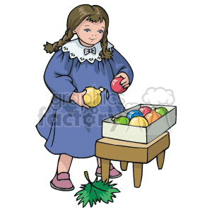   The clipart image features a young girl in a blue dress with a white collar, holding a yellow Christmas bulb in one hand and a red one in the other. She is standing next to a small table or stool which has a box containing colorful Christmas ornaments. There is also a green piece of what appears to be Christmas tree foliage or a holly leaf on the ground near the girl