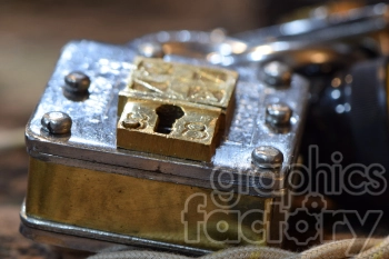 A close-up image of an antique padlock made of brass and steel, featuring a keyhole and distinctive screws.
