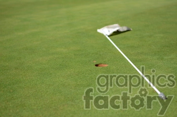 A close-up image of a golf green with a flagstick lying on the ground and a golf hole surrounded by a divot.