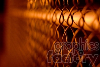 A close-up image of a chain-link fence with a warm, orange glow.