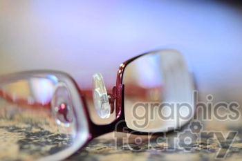 Close-up image of a pair of eyeglasses with a maroon frame placed on a marble surface. The background is blurred, highlighting the glasses' details.