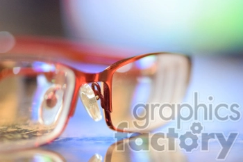 A close-up image of red-frame eyeglasses with a blurred background, showcasing the details of the lenses and frame.