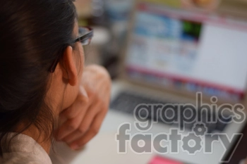 An individual wearing glasses is viewed from behind while they look at a laptop screen showing a blurred webpage.