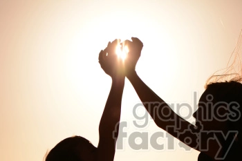 Silhouette of two people reaching towards the sun with their hands joined, creating a heart shape with sunlight shining through.