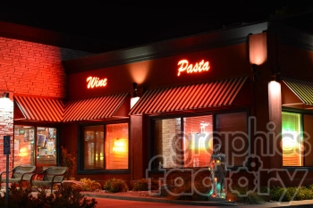 Exterior of a restaurant at night with neon signs that read 'Wine' and 'Pasta'. The building has striped awnings and a stone brick facade, along with visible interior lights. There are two chairs in front and a statue surrounded by plants.
