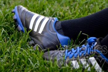 A close-up image of a pair of black and white striped soccer cleats with blue laces and trim on green grass.