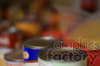 Close-up of canned food items and packaged pasta in a pantry or storage. Blurred background emphasizes the focus on the canned food.
