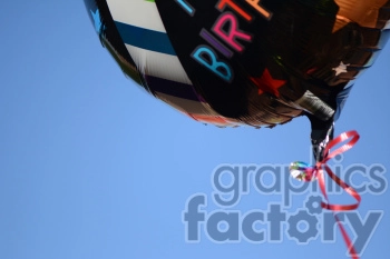 A close-up view of a colorful, striped helium balloon with the word 'Birthday' visible, floating against a clear blue sky.