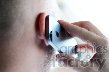 Close-up image of a person holding an iPhone to their ear while making a phone call.