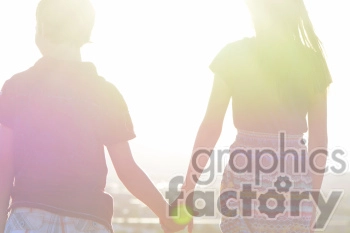 Rear view of two children holding hands with bright sunlight in the background.