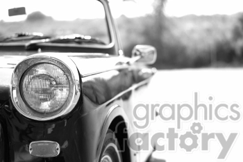 Black and white image of a classic car's front end, focusing on the headlight and a portion of the car's body.