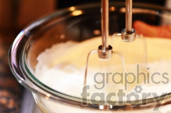 A close-up image of an electric mixer beating ingredients in a clear glass bowl, typically used for baking or cooking.