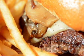 Close-up image of a juicy cheeseburger with melted cheese, grilled mushrooms, and French fries