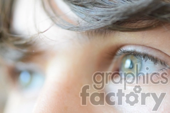Close-up of human eyes with light-colored irises and eyelashes, partially covered by hair.