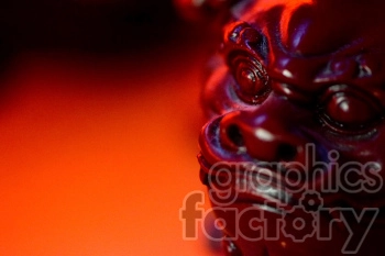 Close-up image of a red Chinese lion statue with a focus on its face, illuminated by red lighting.