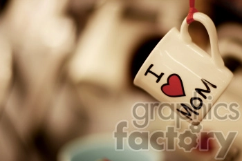 A close-up image of a coffee mug hanging by its handle with the words 'I love Mom' written on it. The background is blurred, focusing the attention on the mug.