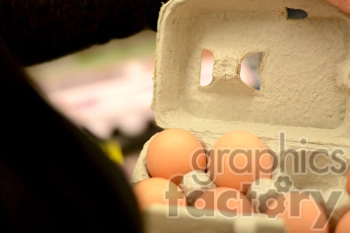 A close-up image of a cardboard egg carton containing six brown eggs, with a hand partially visible holding the carton open.
