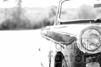 Black and white clipart image of a vintage car focusing on the front headlight and part of the body, with a blurred background.