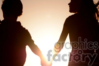 Silhouette of two people holding hands against a setting sun.
