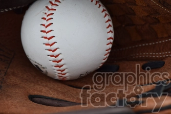 A close-up image of a baseball nestled inside a brown leather baseball glove. The baseball has red stitching and the glove shows detailed texture.