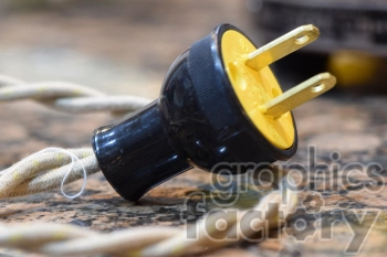 Close-up of a retro electrical plug with a yellow base and black casing attached to a twisted fabric cord on a granite surface.