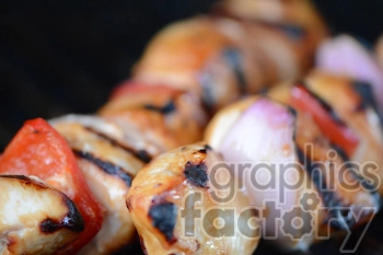 Close-up image of grilled chicken kebabs with vegetables including tomatoes and onions on skewers.