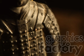 Close-up detail of a textured ancient warrior statue, focusing on the armor and upper body with dark shadows and warm lighting.